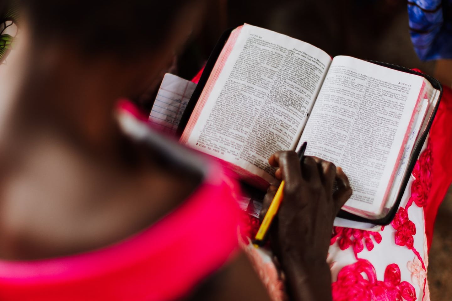 A woman in a floral dress studying an open Bible with a pencil